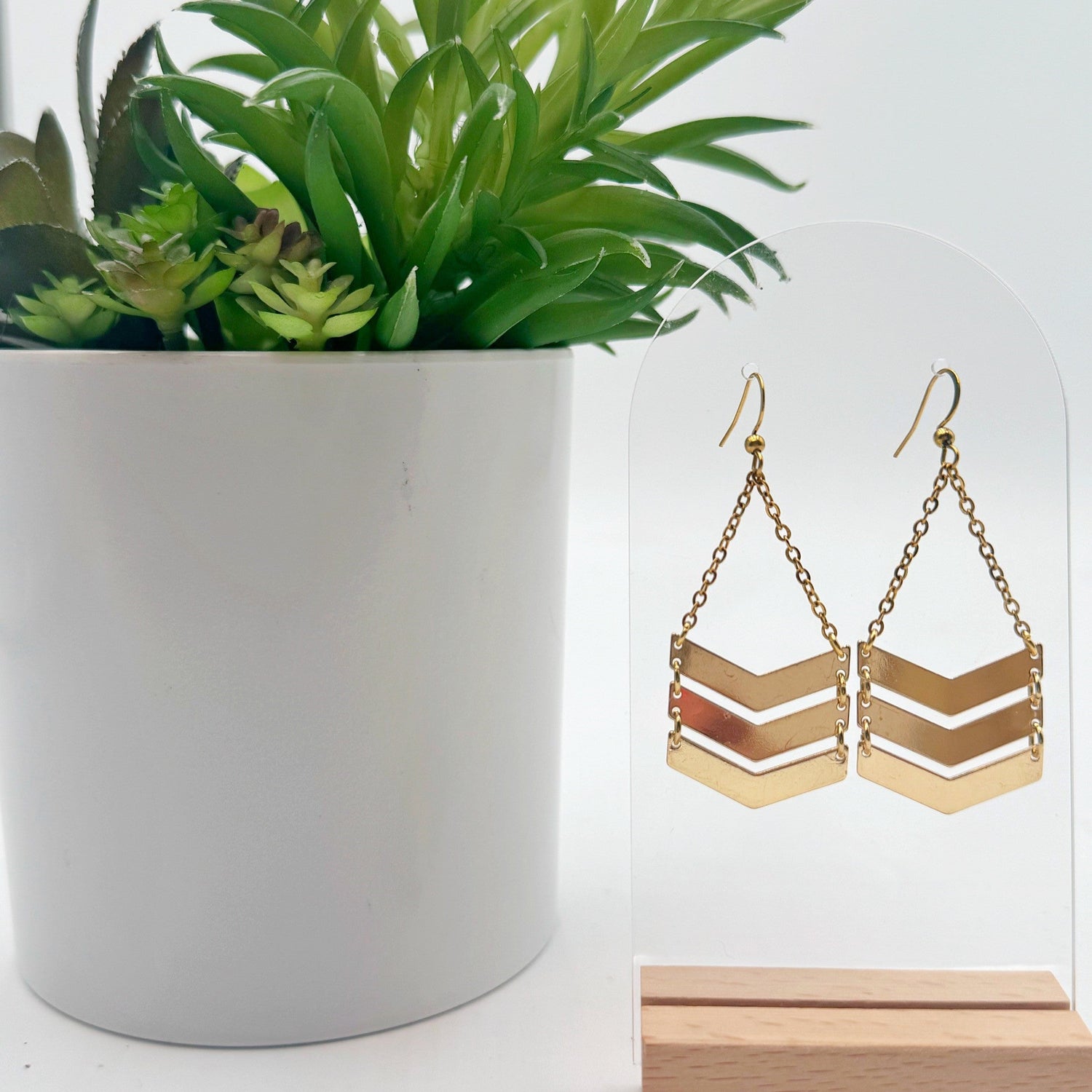 Gold chevron earrings on a stand with a potted plant in the background