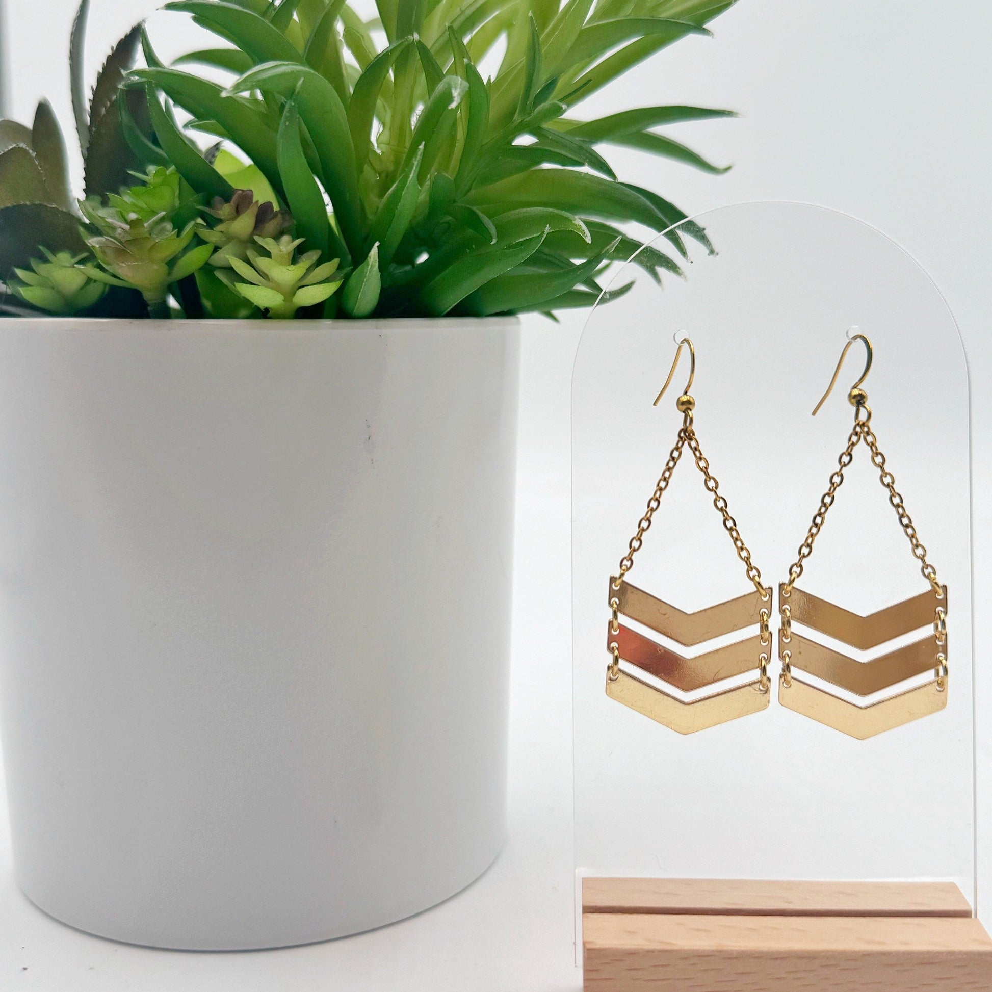 Gold chevron earrings on a stand with a potted plant in the background
